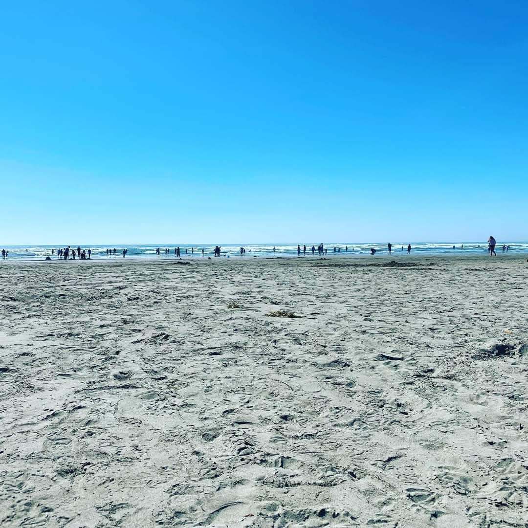 Huge clear blue sky over a wide sandy beach with people at the waterline