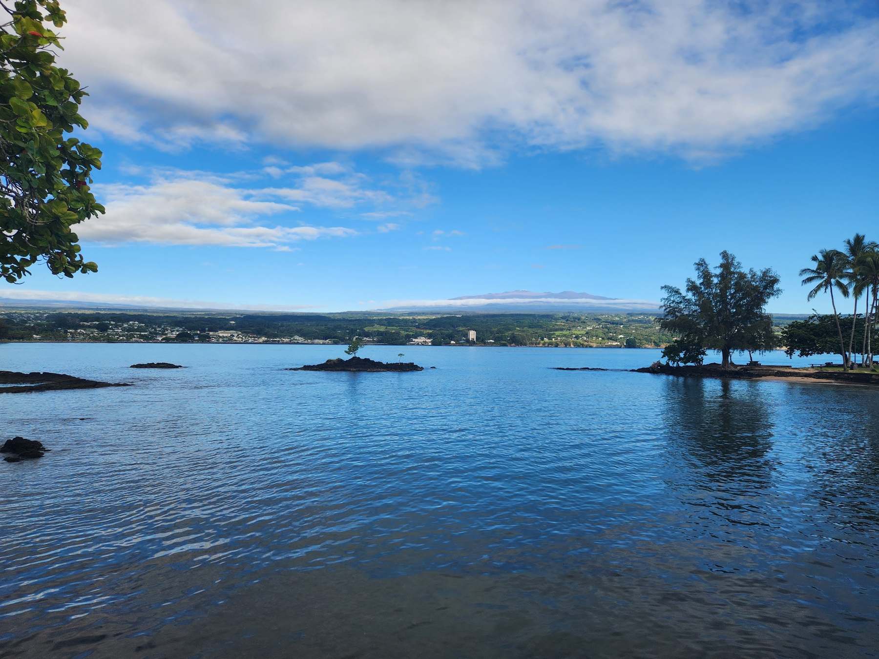 Still blue bay mirroring the sky, small islands and palms along the far shore