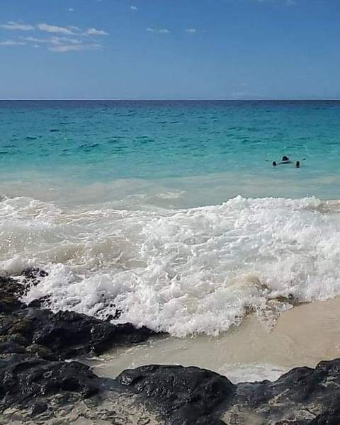 Waves breaking over black rocks onto a sandy beach
